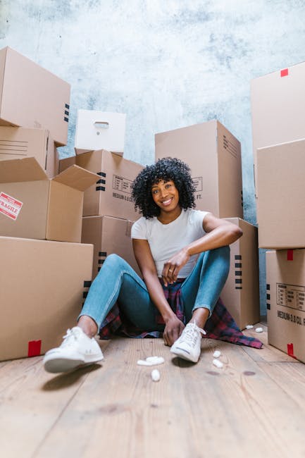 Two movers from Man With a Van Aldgate are engaged in a home relocation process, loading a large piece of furniture covered with a green protective blanket into the back of a white van parked on a res